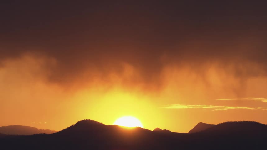 Sun rising behind mountain silhouettes under an orange sky
