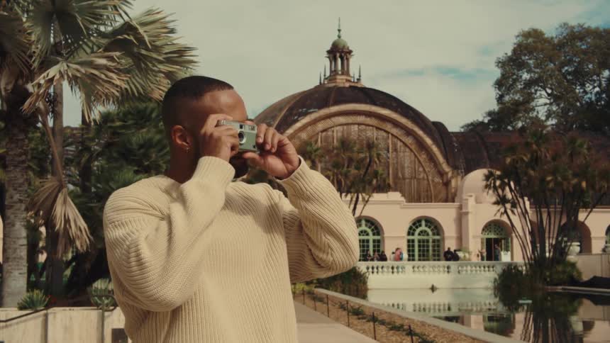A man takes a photo with a camera in front of a botanical building and pond