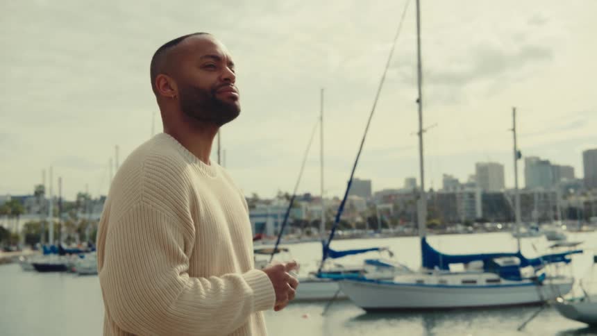 Man looks toward a marina with anchored sailboats and a city in the background