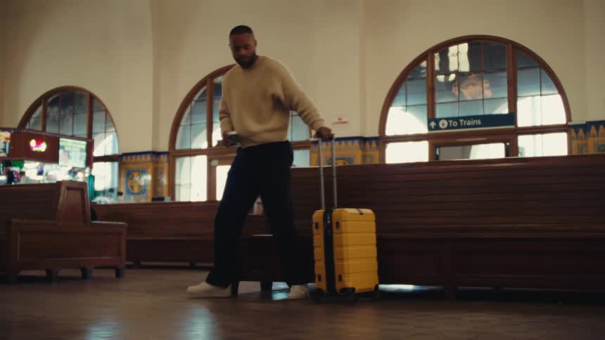 Man walking through a train station pulling a yellow wheeled suitcase