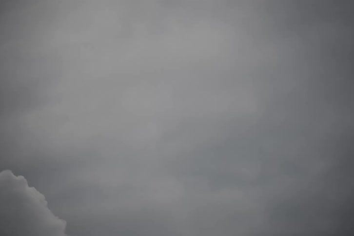 A time lapse view shows dense grey clouds swirling and merging together across a dark and overcast sky during a stormy day