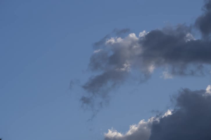 Dark storm clouds moving across a bright blue sky with sunlight on their edges