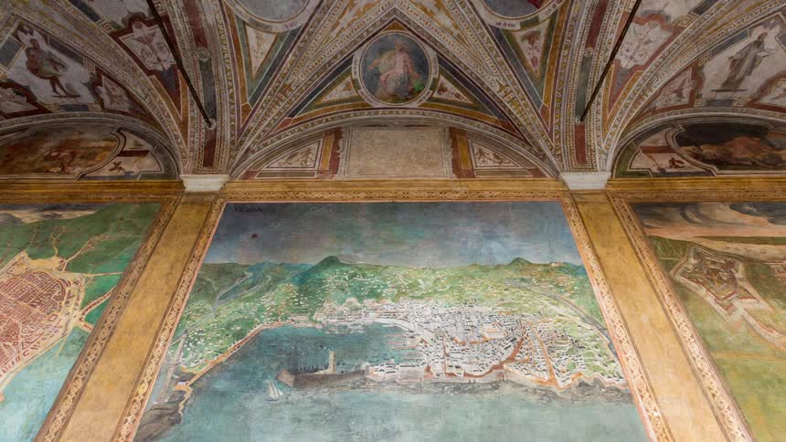 A large detailed fresco of a coastal city map sits beneath a vaulted ceiling adorned with intricate religious paintings the ornate chamber showcases classical renaissancestyle artistry blending cartography with religious and decorative mu