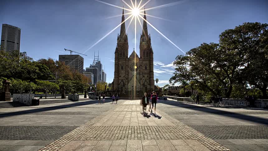 Cathedral with two towers facing a paved square with people walking under strong sunlight