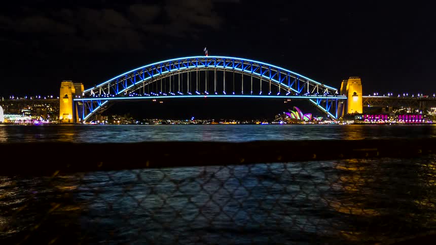 Boats and a bridge are lit up at night in a city