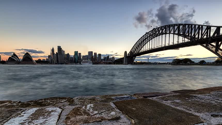 A bridge spanning a river leading to the city as daylight turns into nighttime
