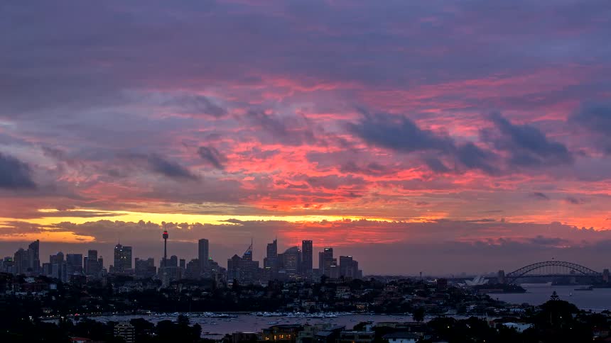 A wide shot of the sydney skyline and harbour bridge silhouetted against a vivid purple and orange sunset