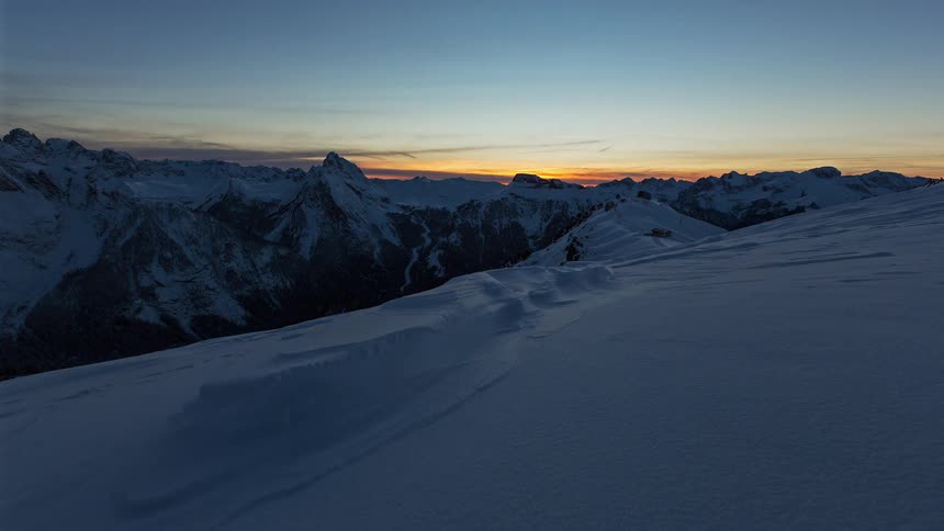 Snowcovered mountain range with the sun setting on the horizon