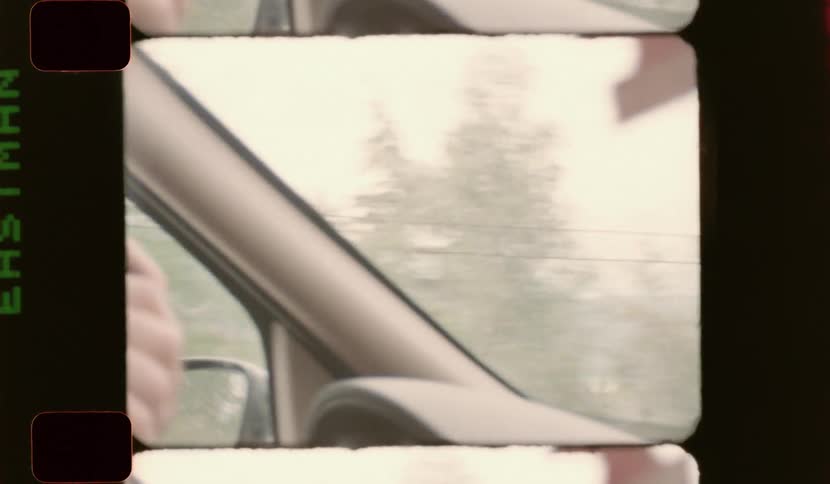 Hand holding a steering wheel inside a moving car with blurred trees in the background