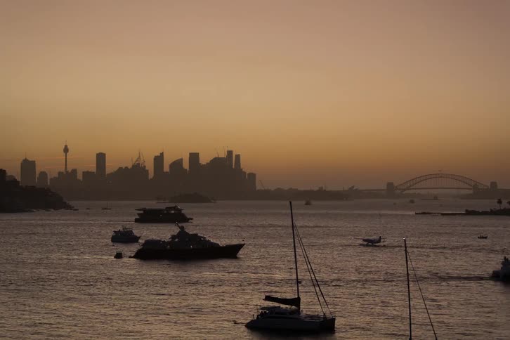 Sunrise glowing behind a city skyline with boats silhouetted in the harbor