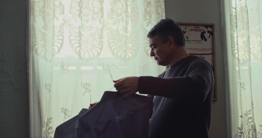 Man standing in a room holding up two shirts trying to decide which one to wear