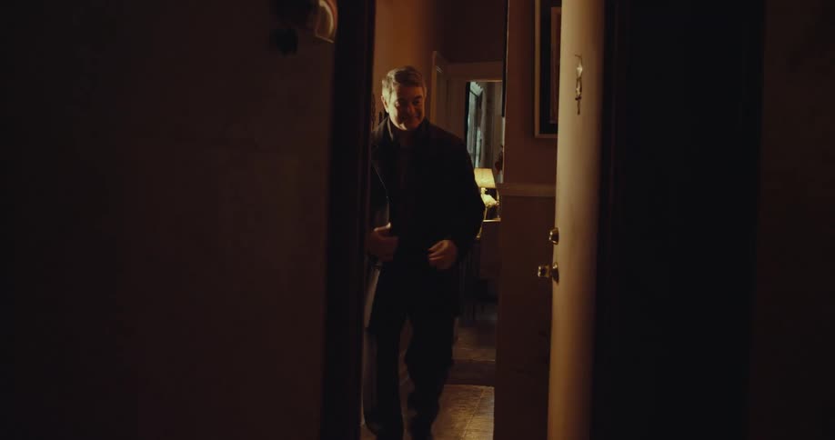 Man enters dark room through partially open door lit by interior light