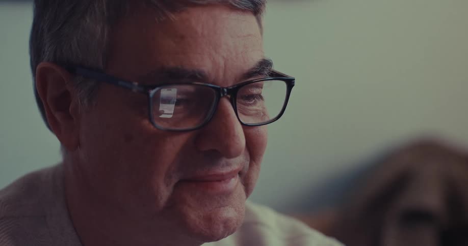 Closeup of an older man smiling while scrolling through memories on a smartphone indoors