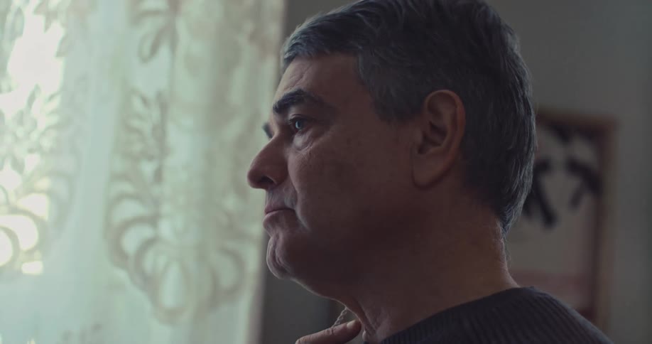 Man observes clothes near a window with a patterned curtain