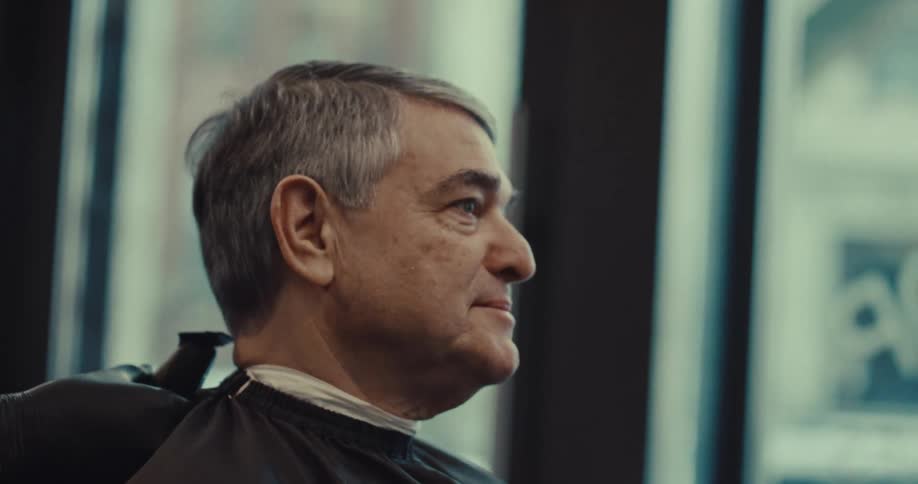 Man sits in the barbershop as the barber combs his hair and cuts it with an electric razor