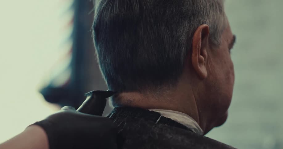 Man sits in the barbershop as the barber combs his hair and cuts it with an electric razor