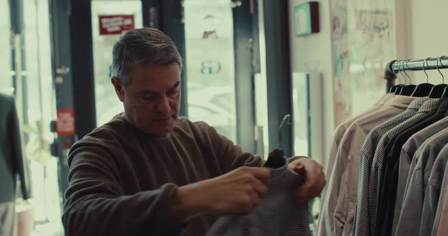 A man standing in clothing off the rack and holds it up to himself