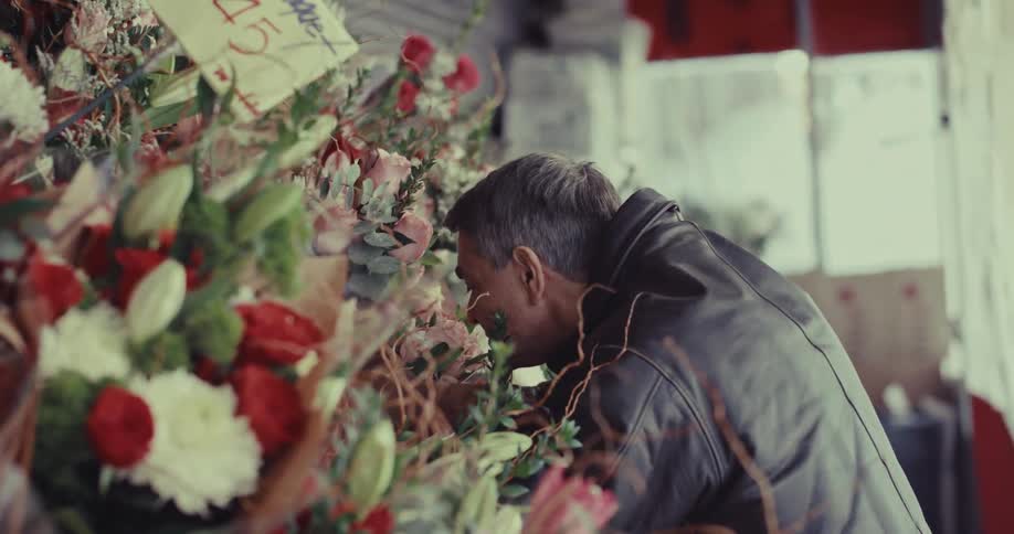 Man in leather jacket places flowers at memorial covered with bouquets and messages
