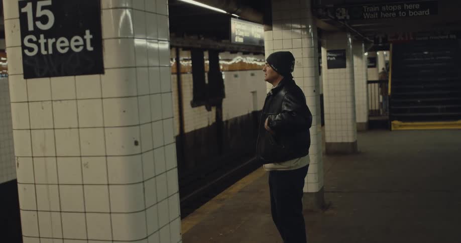 A man checking his phone while waiting for a train on a subway platform