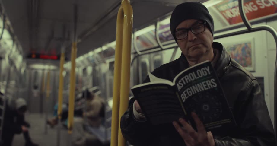 A man standing and reading an astrology book while commuting on a subway train