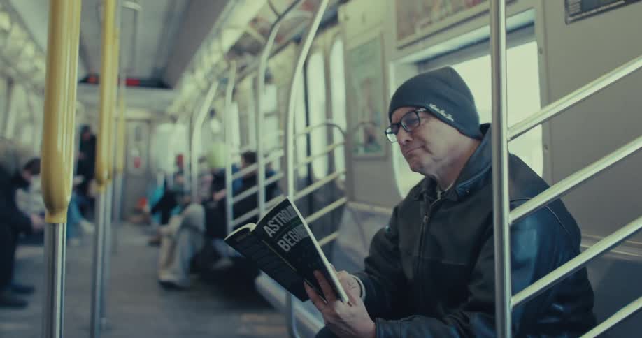Man sitting in subway car reads book while holding metal pole