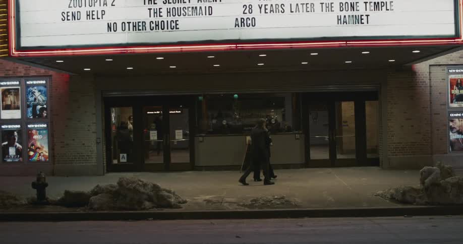 A man and woman hug in front of a movie theater and enter together