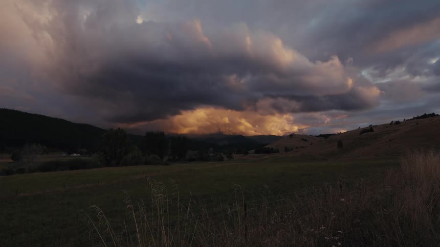 Dense clouds over hills and open field illuminated by evening light