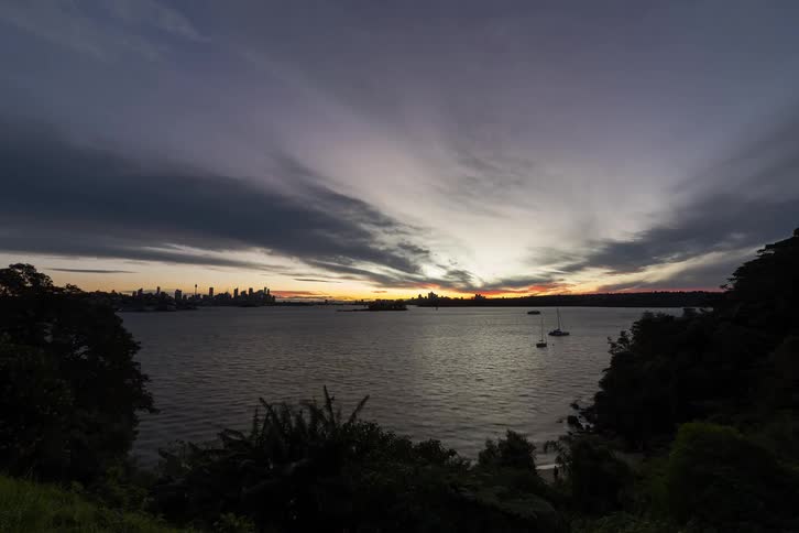 Nightfall over bay with anchored sailboat and illuminated city skyline in the distance