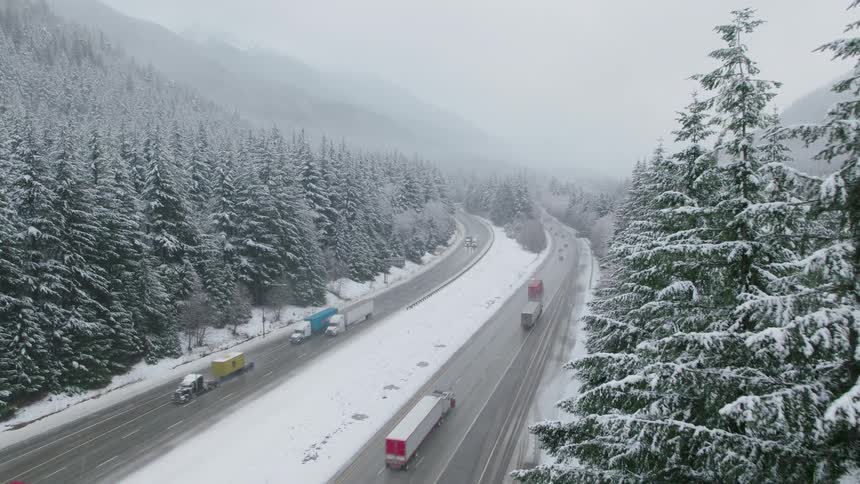 Interstate traffic winds through the valley of a mountain pass as falling snow blankets the landscape