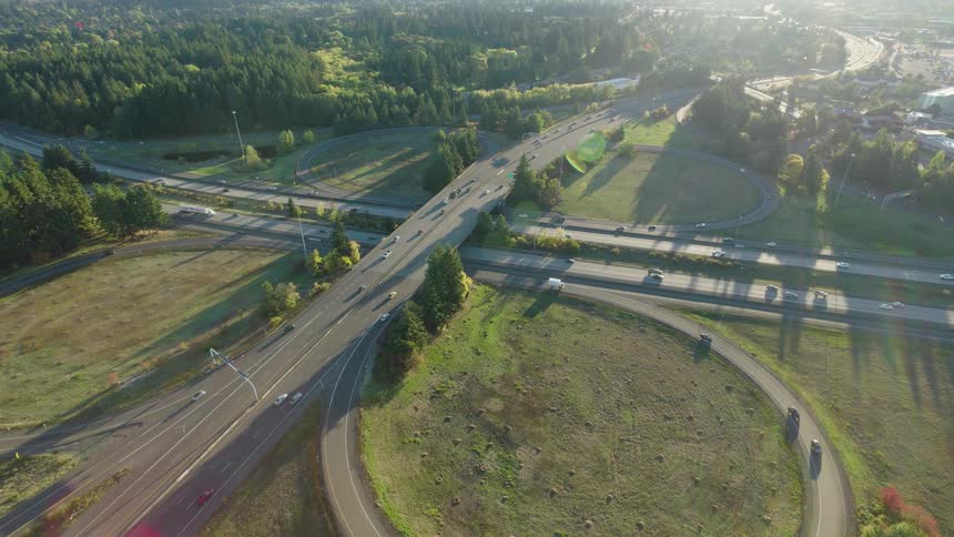 Sunshine rakes across a classic highway interchange cloverleaf with light traffic