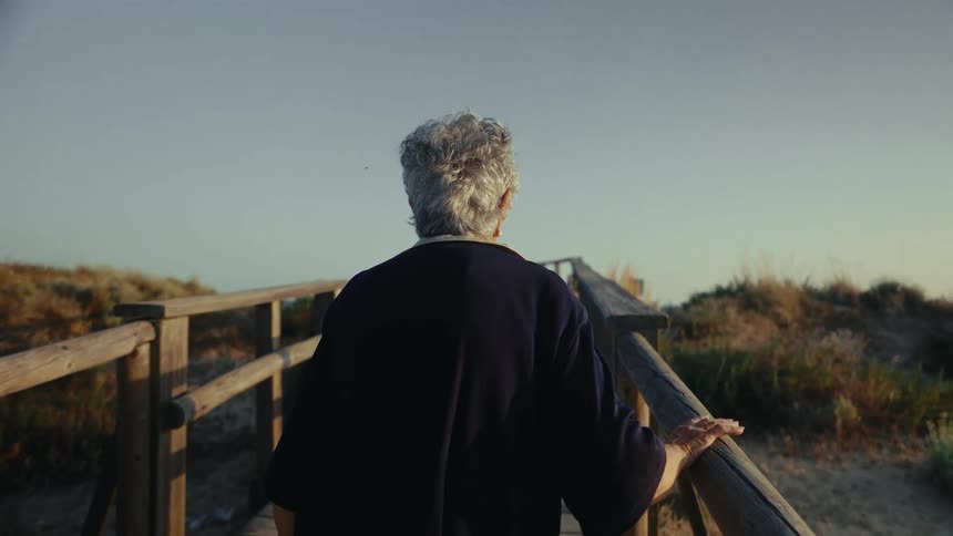 Elderly woman walks along a wooden path passing over short hills during the daytime