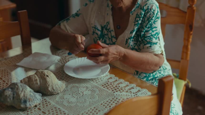 Elderly woman sits at her table and peels a piece of fruit