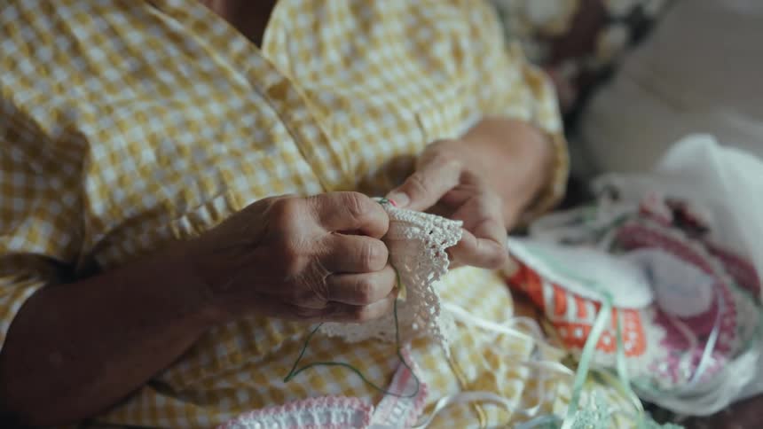 A persons hands skillfully working on a piece of delicate white lace using a small crochet hook and green threadin the background several other colorful textile projects and materials are visible highlighting a focused and creative crafting environm