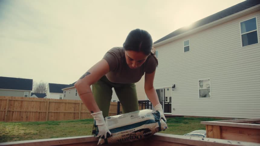 Woman cuts open a bag of soil for her backyard garden