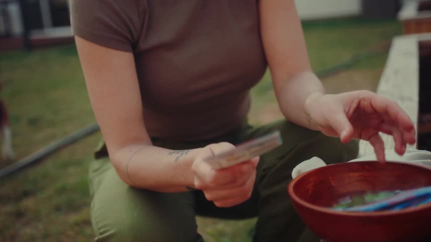 A woman sorts seed packets into a wooden bowl while kneeling in a garden