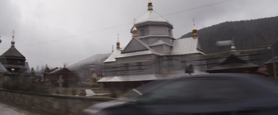 Wooden church with golden domes seen beside a road in a mountainous area
