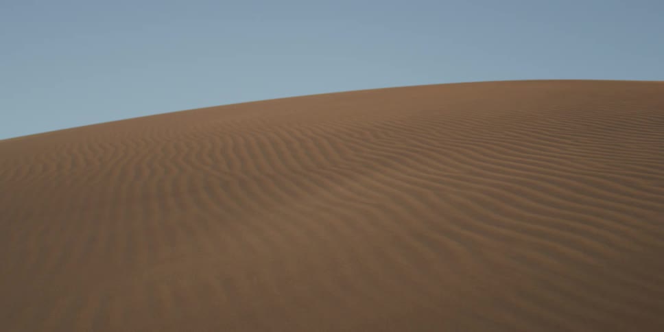 Sand ripples form patterns across a dune under blue sky