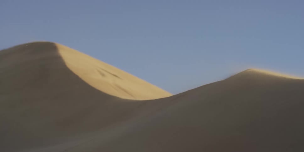 Sand blows through the air passing desert dunes during the daytime