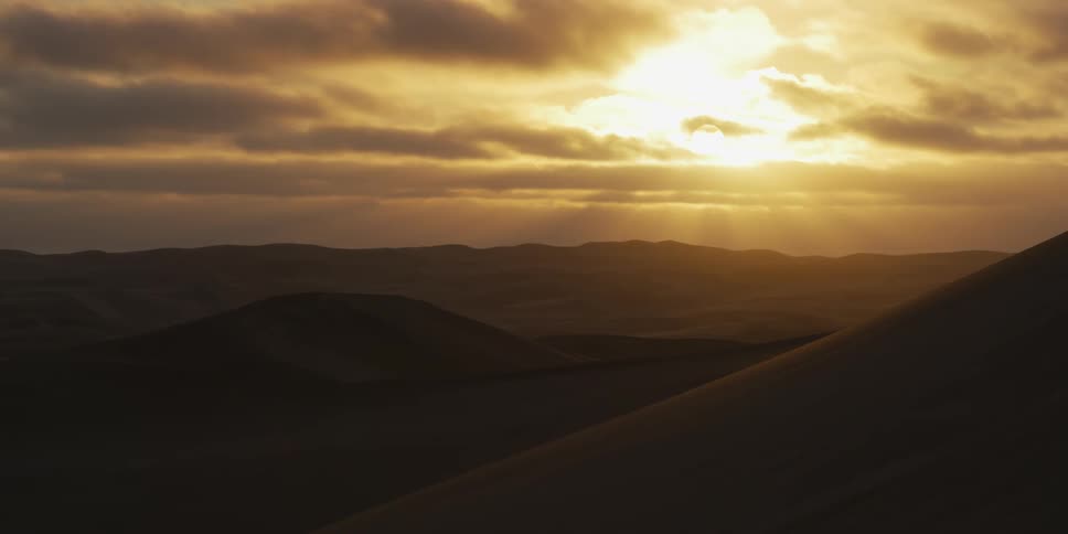 Mountains across the desert landscape as the sun shines brightly through clouds in an orange sky