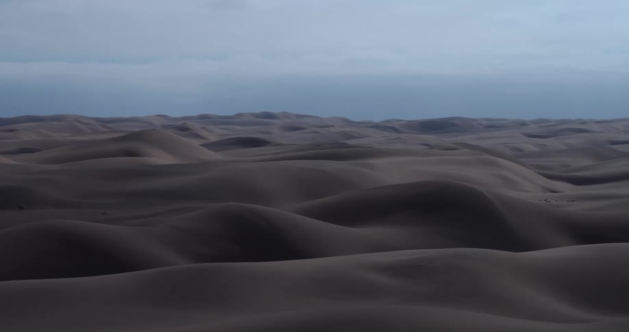 Silhouettes in a dip in the desert contrast with the sand under an overcast sky