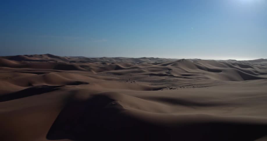 Dunes across the desert landscape as the sun shines from above
