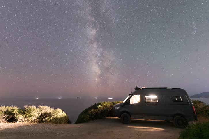 Van parked on coastal cliff under starry sky with the milky way visible