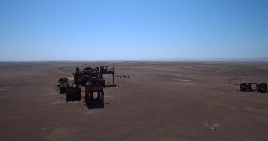 An aerial view shows the rusty remains of the abandoned oil drilling rig at the skeleton coast in namibia sitting on the flat desert sand under a clear blue sky