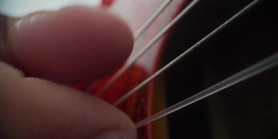 A close view shows the fingers of a person plucking the nylon and metal strings of an acoustic guitar with a decorative orange sound hole rosette