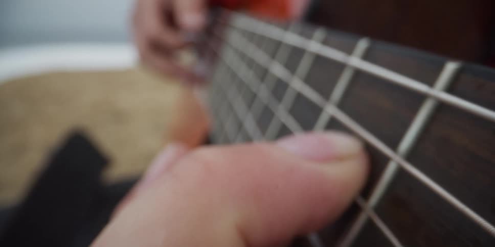 Musician holds their fingers on the fretboard and strums the strings of an acoustic guitar