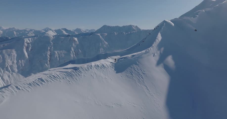 A person walks along a snow ridge in the mountains