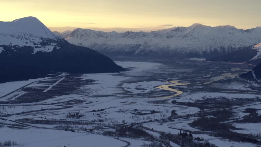 Snow covered mountains across the landscape with a river in the valley under a cloudy sky