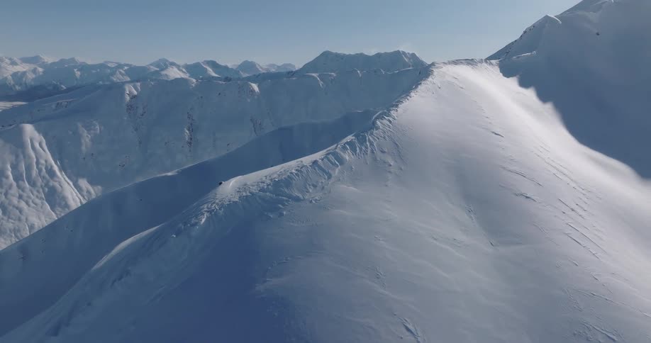 An aerial view shows the vast snow covered peaks of the chugach mountains in alaska under a clear blue sky during a bright winter day