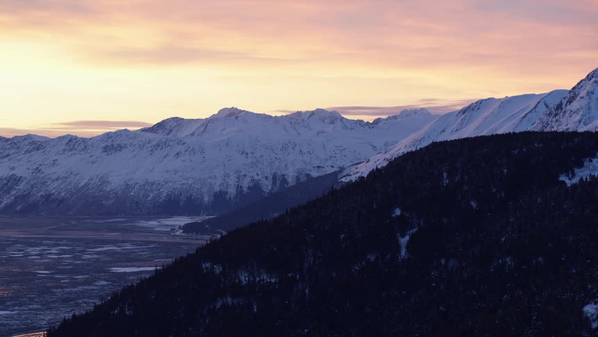 Forested mountain overlooking the valley with snow covered mountains in the distance