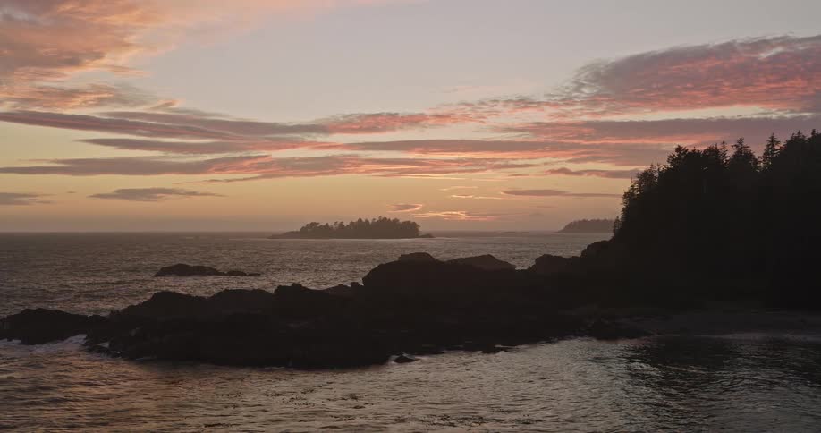 An aerial view reveals a rugged coastline during a vibrant and colorful sunset over the ocean